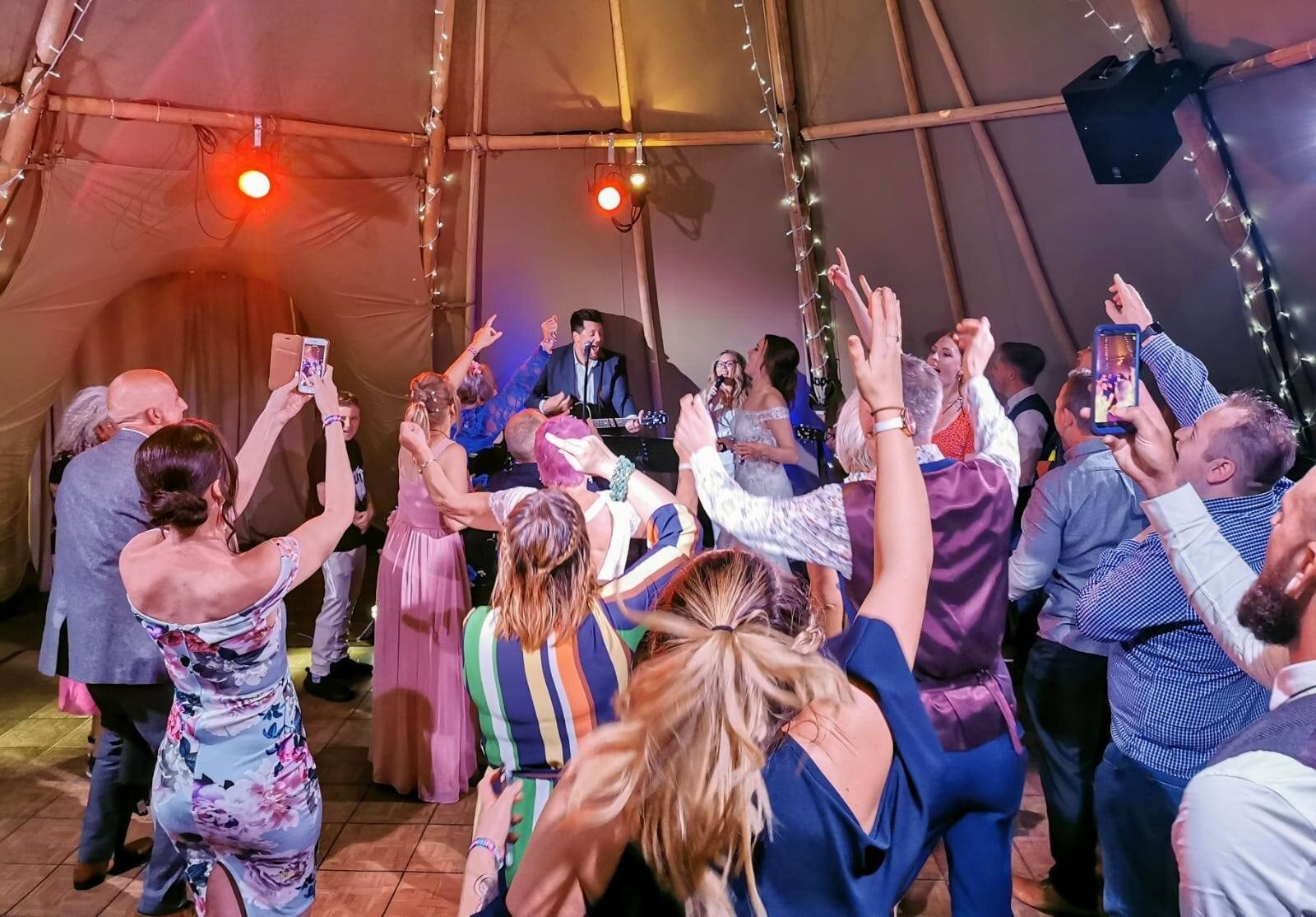 A packed wedding dance floor with guests raising their hands
